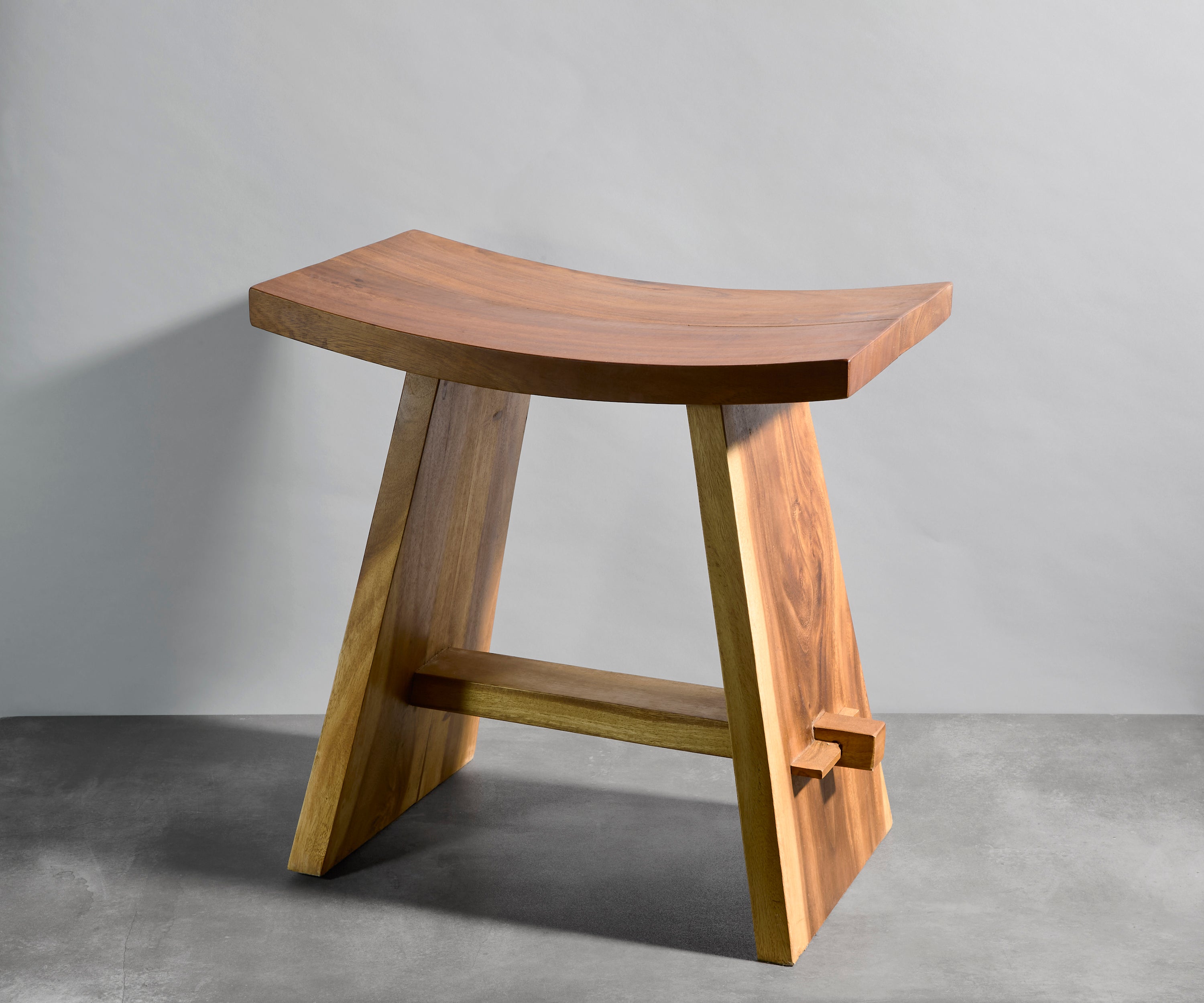 Wooden stool with curved top and straight legs on a gray background