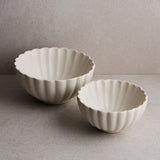 Two white ceramic bowls with fluted edges on a gray surface.
