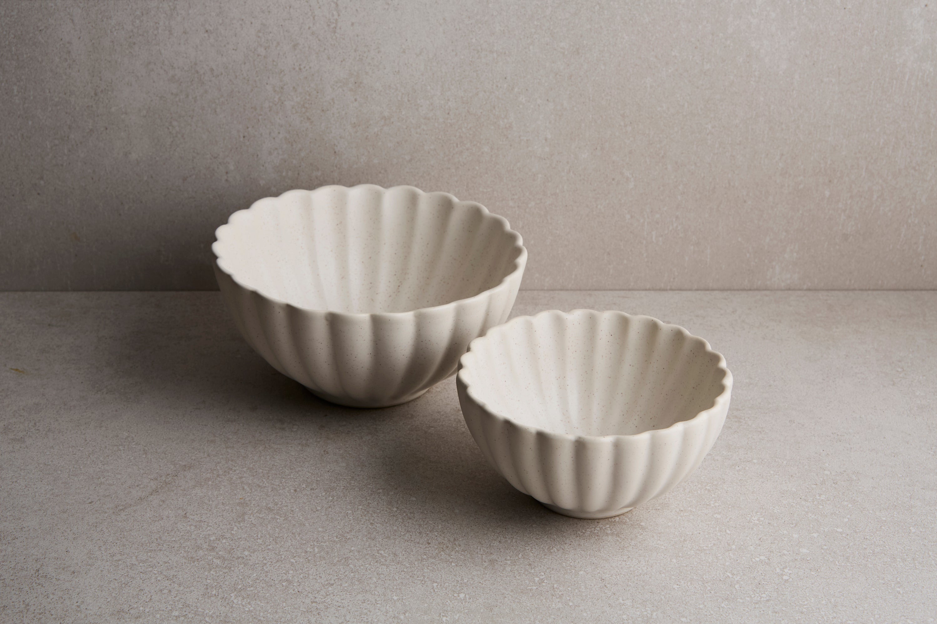 Two white ceramic bowls with fluted edges on a gray surface.