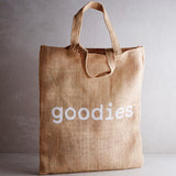 A brown jute tote bag with the word 'goodies' printed in white on the side.
