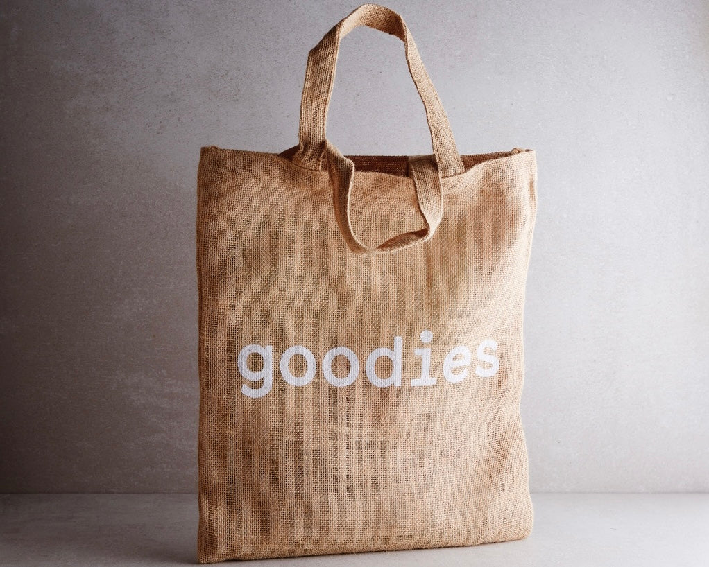 A brown jute tote bag with the word 'goodies' printed in white on the side.